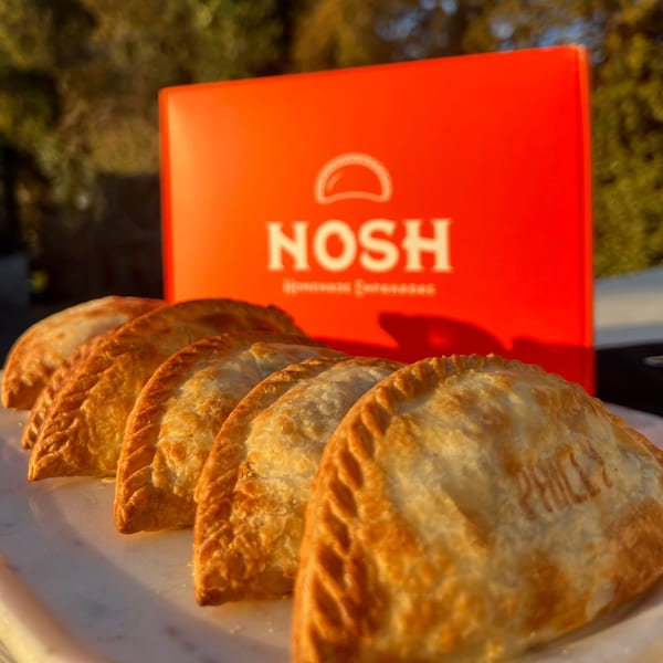 Golden-brown Nosh Empanadas arranged on a white platter with a red Nosh box in the background.