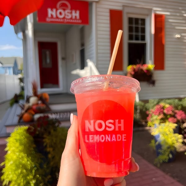 Hand holding a Nosh Lemonade cup in front of the Nosh Empanadas restaurant.